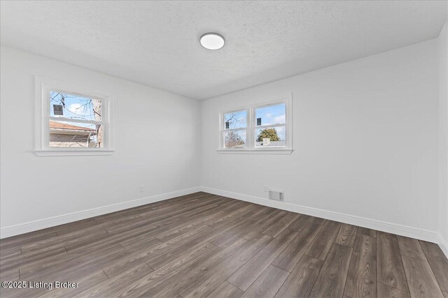 empty room with dark wood-type flooring, baseboards, visible vents, and a textured ceiling