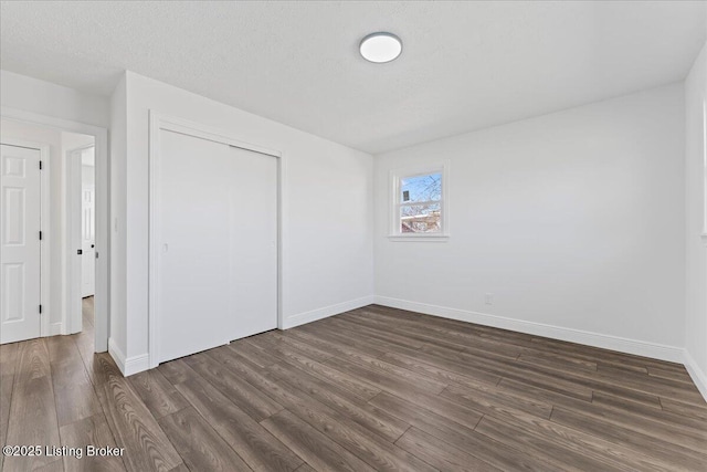 unfurnished bedroom with a closet, baseboards, and dark wood-style flooring