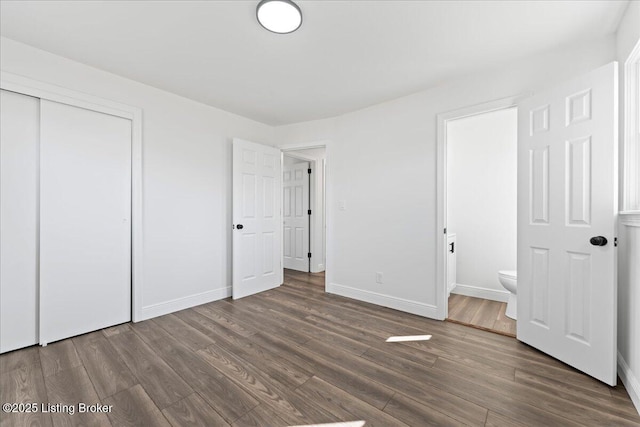 unfurnished bedroom featuring a closet, ensuite bathroom, baseboards, and wood finished floors