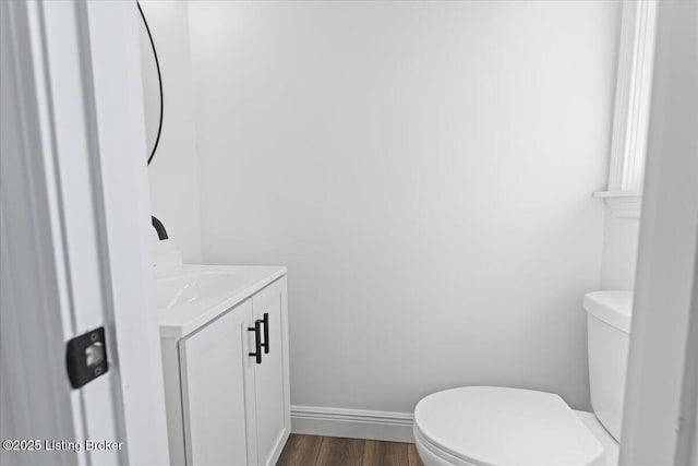 bathroom featuring toilet, vanity, baseboards, and wood finished floors