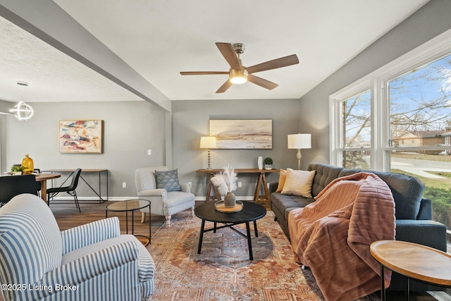 living area with ceiling fan with notable chandelier, baseboards, and wood finished floors