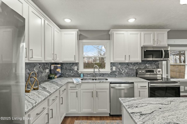 kitchen with light stone counters, dark wood-style flooring, a sink, white cabinets, and appliances with stainless steel finishes