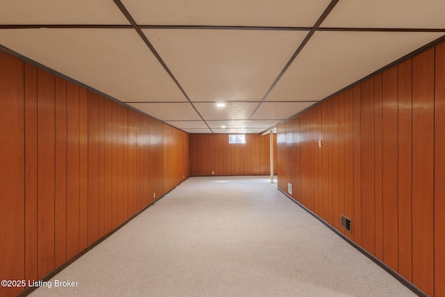 finished below grade area with light colored carpet, visible vents, wood walls, and a paneled ceiling