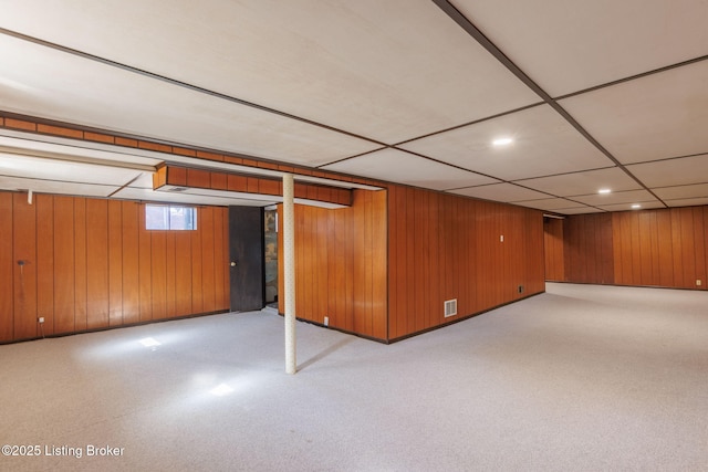 below grade area featuring a paneled ceiling, wooden walls, visible vents, and recessed lighting