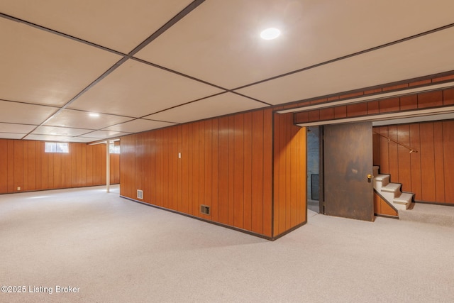 below grade area with a drop ceiling, carpet floors, wood walls, visible vents, and stairs