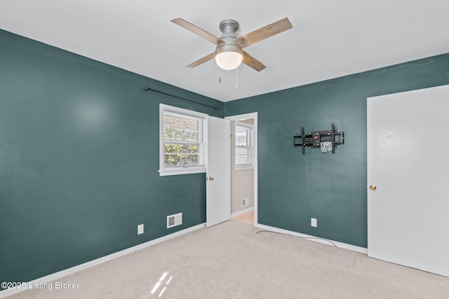 carpeted empty room with ceiling fan, visible vents, and baseboards