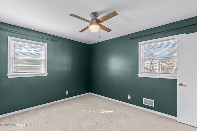 carpeted spare room with a ceiling fan, visible vents, and baseboards