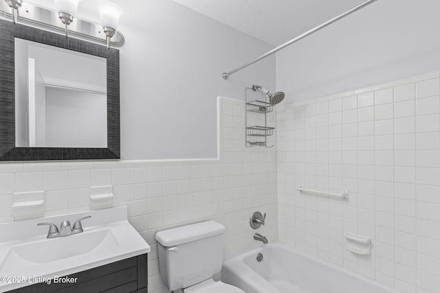 full bathroom featuring toilet, vanity, bathing tub / shower combination, tile walls, and wainscoting