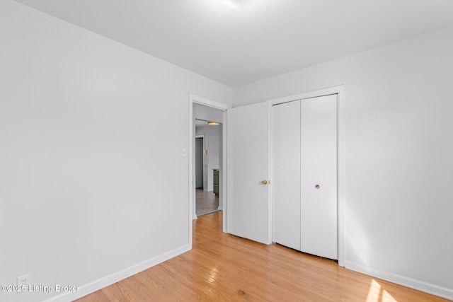 unfurnished bedroom featuring light wood-type flooring, baseboards, and a closet