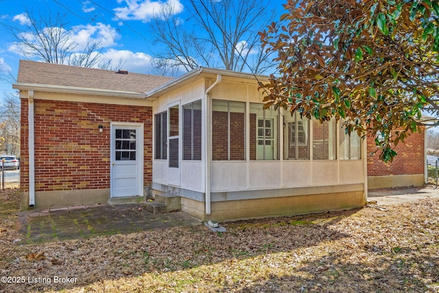 view of side of home featuring a sunroom, brick siding, and roof with shingles