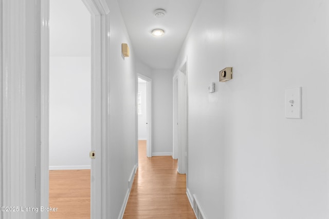 corridor with light wood-type flooring, baseboards, and visible vents