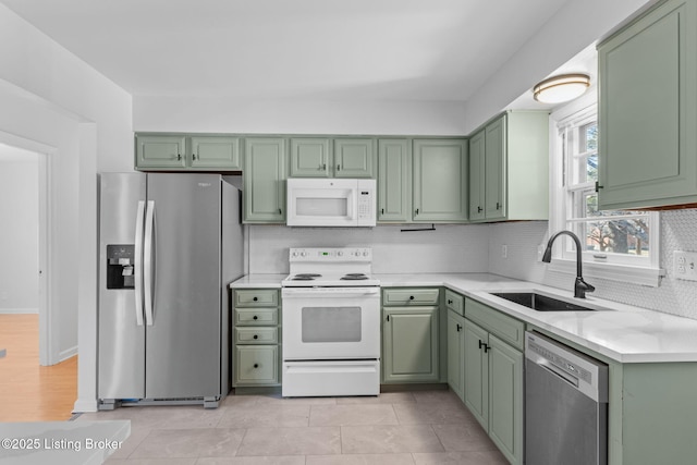 kitchen with a sink, stainless steel appliances, light countertops, green cabinets, and backsplash