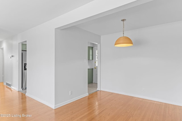 empty room with light wood finished floors, baseboards, and visible vents