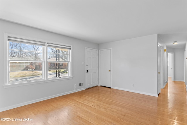 empty room with light wood-style floors, visible vents, and baseboards