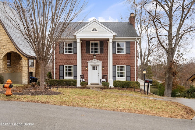 neoclassical / greek revival house with stone siding, a chimney, a front lawn, and brick siding