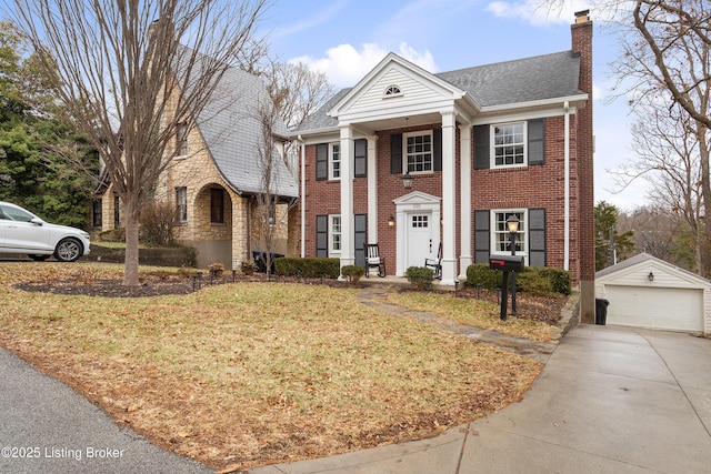 greek revival inspired property with brick siding, a detached garage, a chimney, a front yard, and an outdoor structure