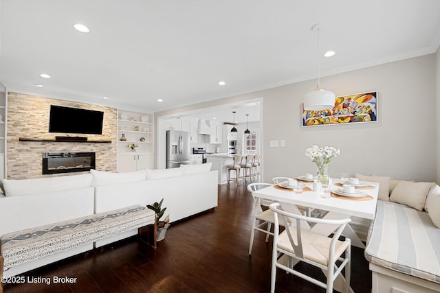 interior space featuring a stone fireplace, recessed lighting, built in features, ornamental molding, and dark wood finished floors