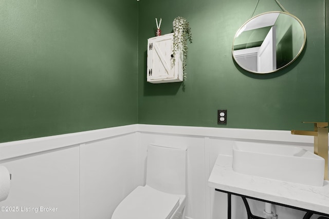 half bath featuring a wainscoted wall, a sink, and toilet