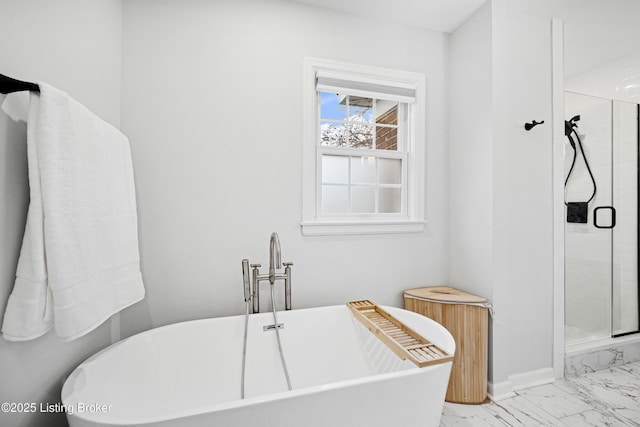 bathroom featuring marble finish floor, a freestanding bath, a shower stall, and baseboards