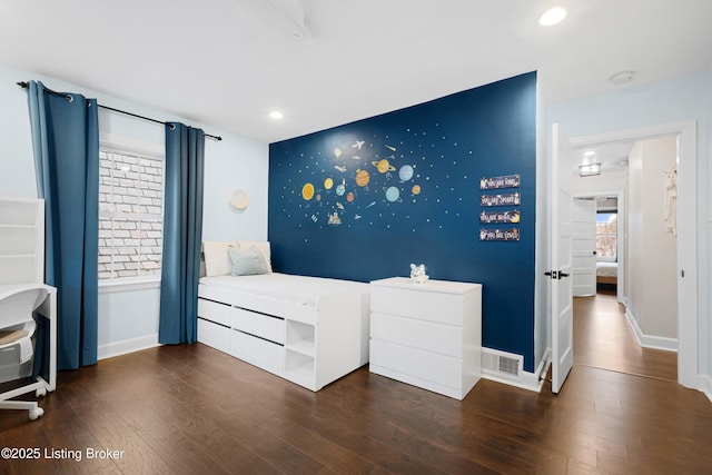 bedroom featuring wallpapered walls, an accent wall, baseboards, and wood finished floors