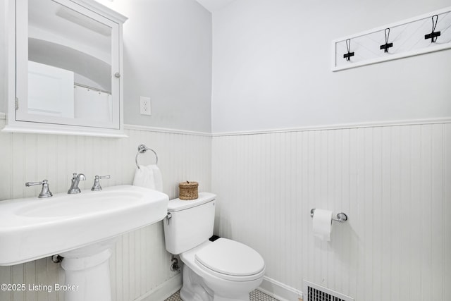 bathroom with toilet, wainscoting, a sink, and visible vents