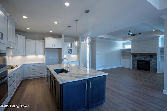 kitchen featuring a stone fireplace, dark wood-style flooring, a sink, and white cabinets