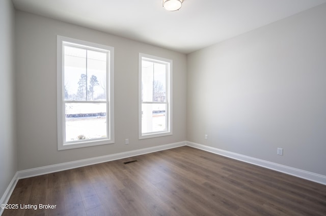 unfurnished room with dark wood-style floors, visible vents, and baseboards