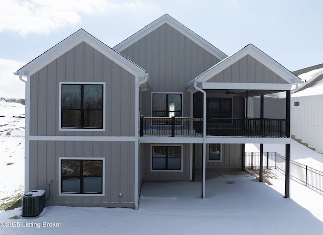 snow covered property featuring board and batten siding, a sunroom, fence, and central AC unit