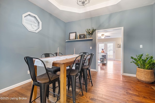 dining room with ceiling fan, baseboards, a raised ceiling, and wood finished floors