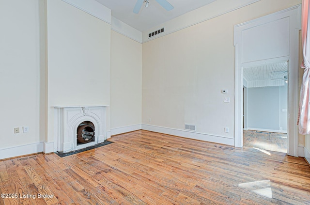 unfurnished living room featuring a fireplace with flush hearth, visible vents, ceiling fan, and wood finished floors