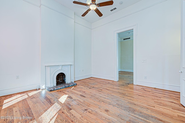 unfurnished living room with visible vents, a fireplace with raised hearth, baseboards, ceiling fan, and wood-type flooring