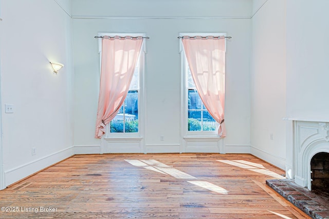 unfurnished living room featuring a fireplace with raised hearth, wood finished floors, and baseboards