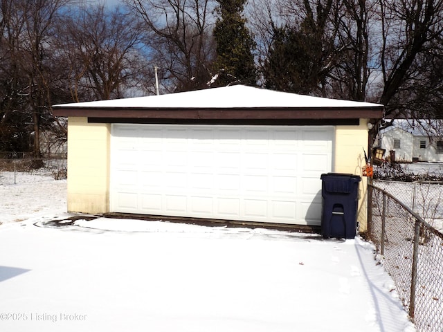 snow covered garage featuring a detached garage and fence