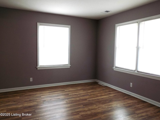 empty room with dark wood-style floors, visible vents, and baseboards