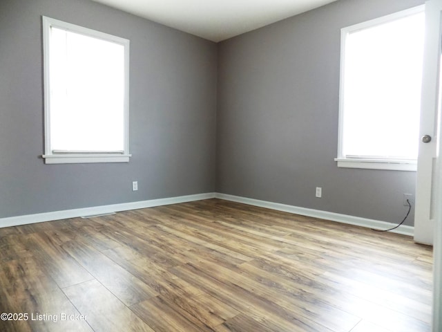 unfurnished room featuring wood finished floors, visible vents, and baseboards