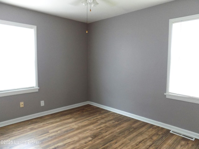 unfurnished room featuring dark wood finished floors, visible vents, plenty of natural light, and baseboards