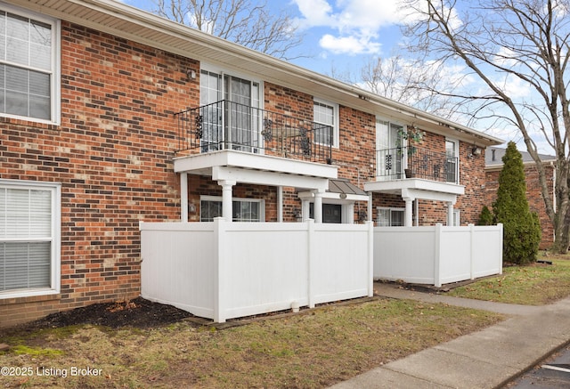 view of front of house featuring a balcony, fence, and brick siding