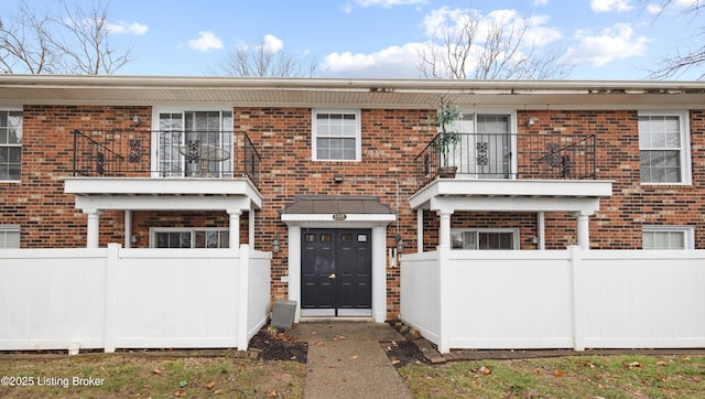 view of property featuring brick siding, fence, and a balcony