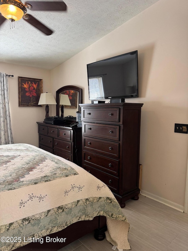 bedroom with a textured ceiling, a ceiling fan, and baseboards