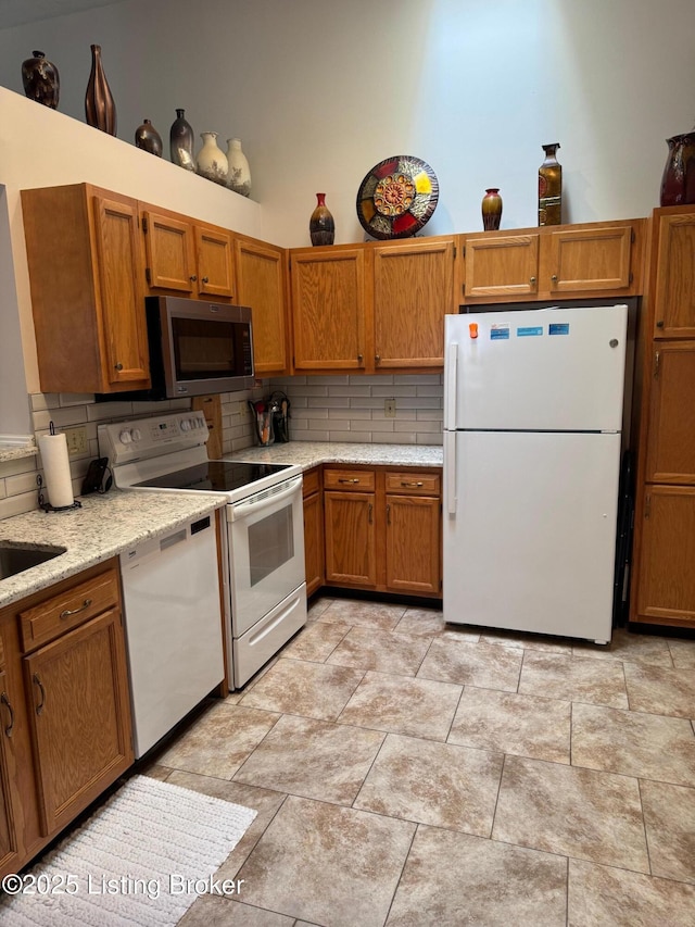 kitchen featuring white appliances, backsplash, light stone counters, and brown cabinets