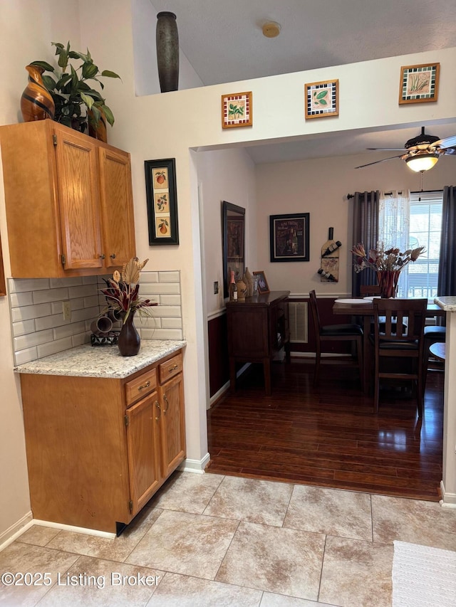 interior space featuring baseboards, decorative backsplash, a ceiling fan, light stone counters, and light wood-type flooring