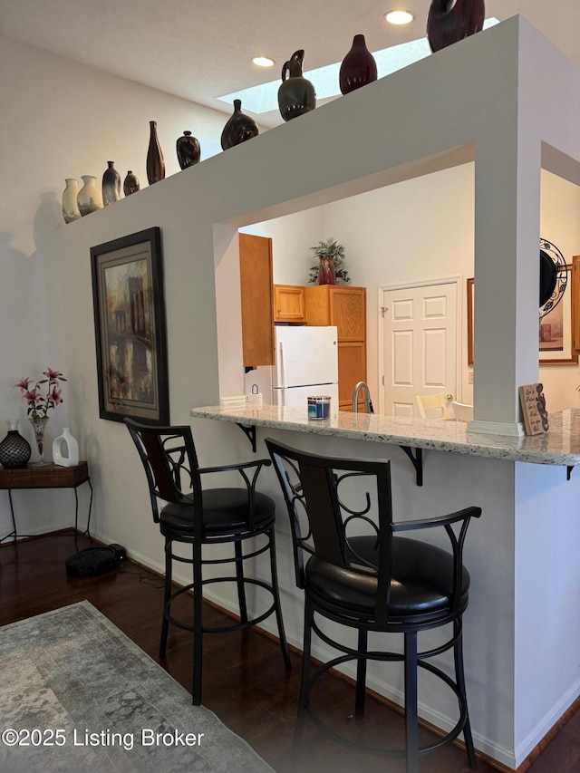 kitchen featuring freestanding refrigerator, dark wood-style flooring, a peninsula, and a breakfast bar area