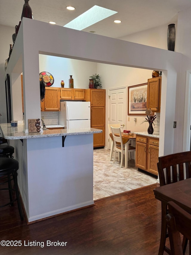kitchen featuring a breakfast bar area, light stone countertops, a peninsula, freestanding refrigerator, and brown cabinets