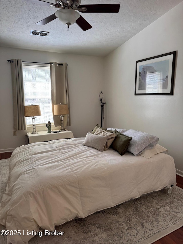 bedroom featuring visible vents, a ceiling fan, vaulted ceiling, a textured ceiling, and wood finished floors
