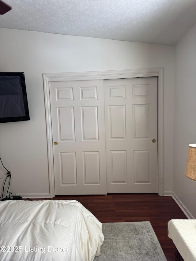 bedroom with dark wood-style floors, a closet, baseboards, and a textured ceiling