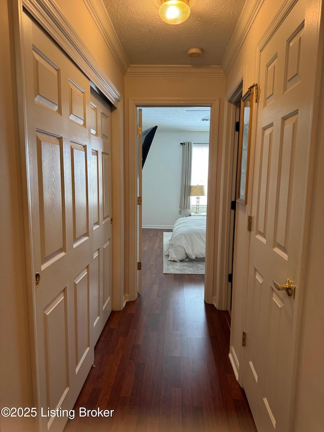 hallway with a textured ceiling, dark wood-style flooring, and crown molding