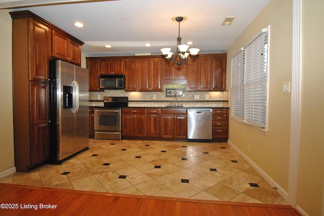 kitchen featuring light wood-style flooring, hanging light fixtures, appliances with stainless steel finishes, backsplash, and an inviting chandelier