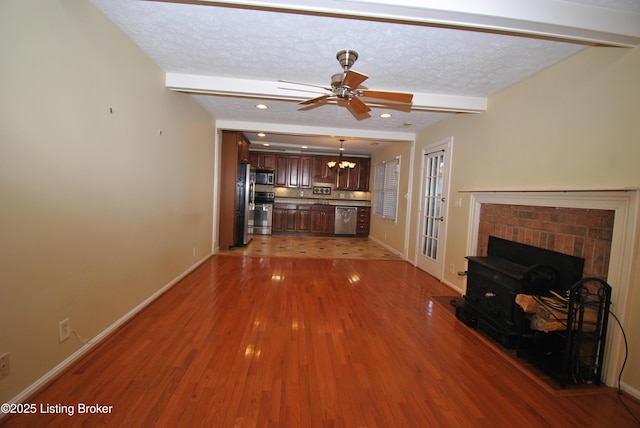 unfurnished living room featuring light wood-style floors, beamed ceiling, a textured ceiling, and baseboards