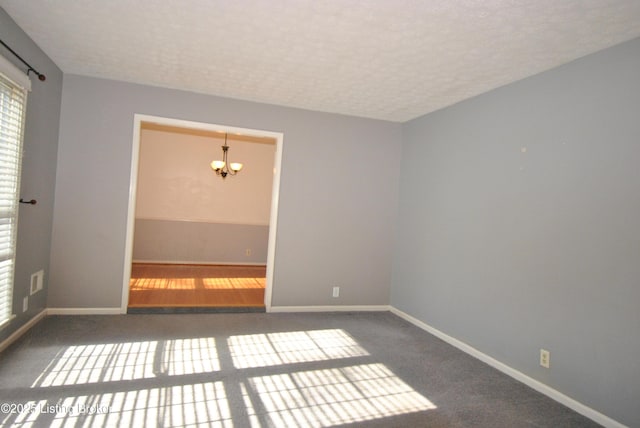 carpeted empty room featuring a notable chandelier, a textured ceiling, and baseboards