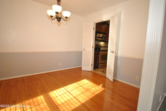 unfurnished room featuring an inviting chandelier, baseboards, and wood finished floors